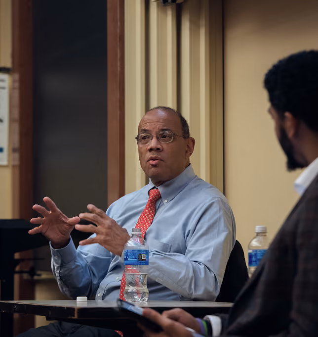 Guest speaker in a red tie gesturing while speaking with a student