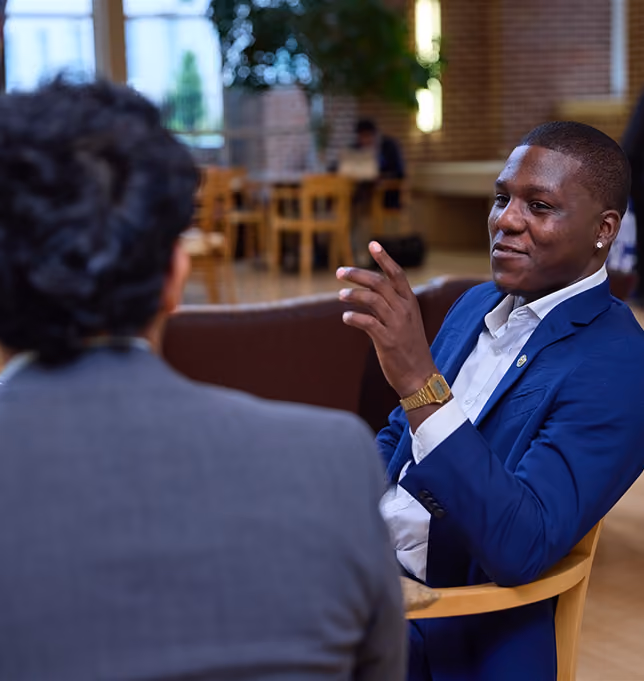 Student in a blue blazer gesturing while in conversation with a peer