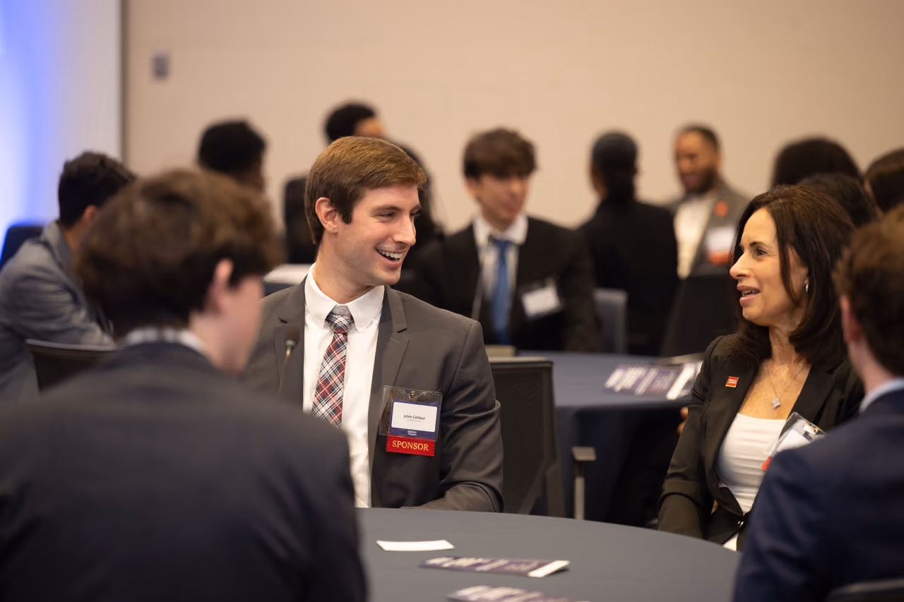 Student wearing a sponsor badge laughing with a professional at a conference table