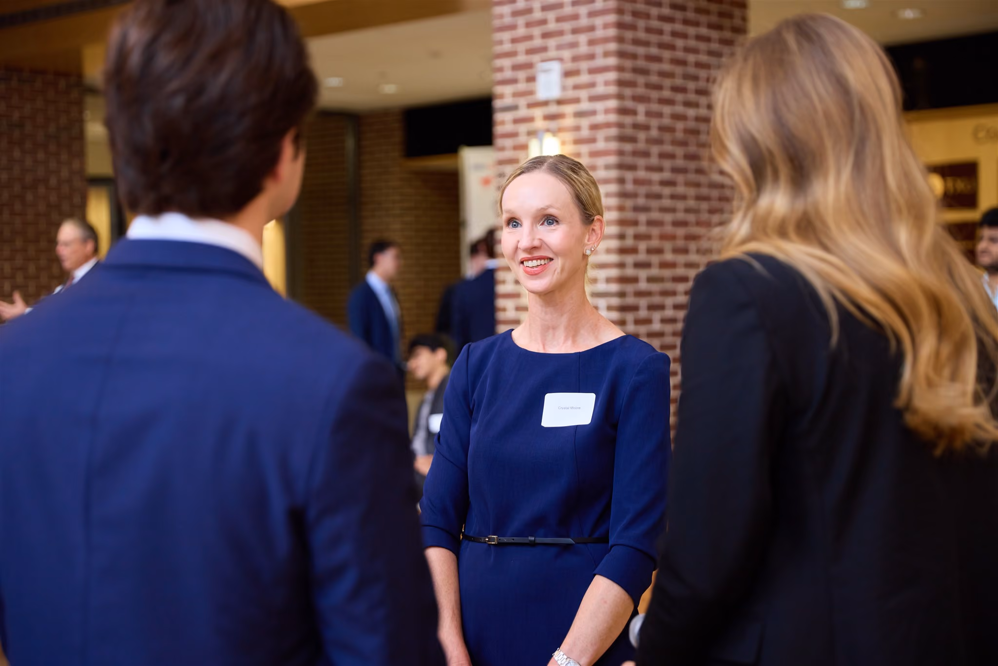 Smiling professional in a navy dress speaking with students at a networking reception
