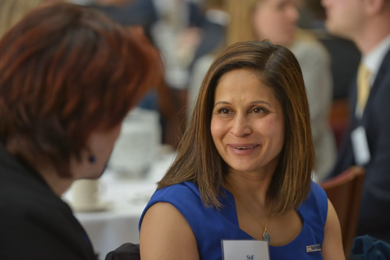 Smiling professional in a blue dress speaking with an attendee at a luncheon