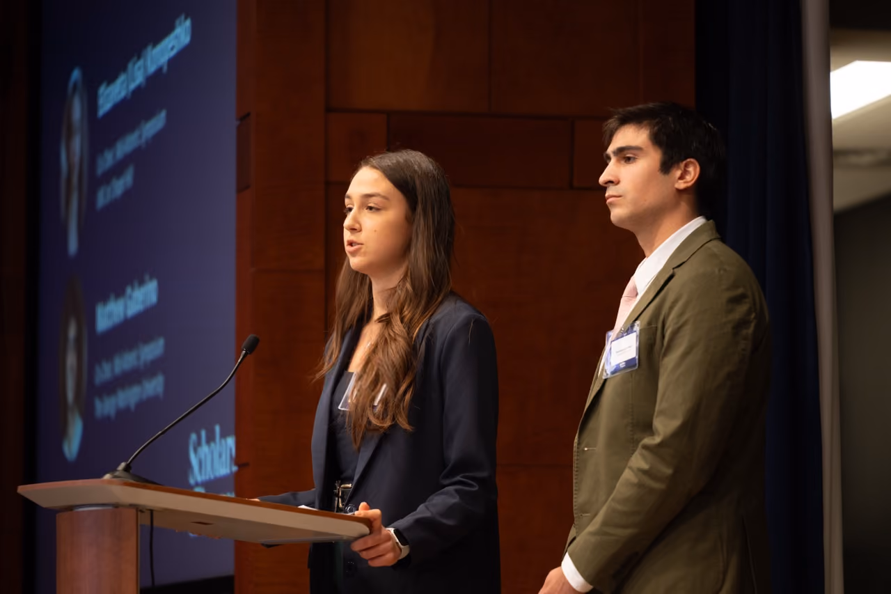 Two students presenting at a podium in front of a projected slide
