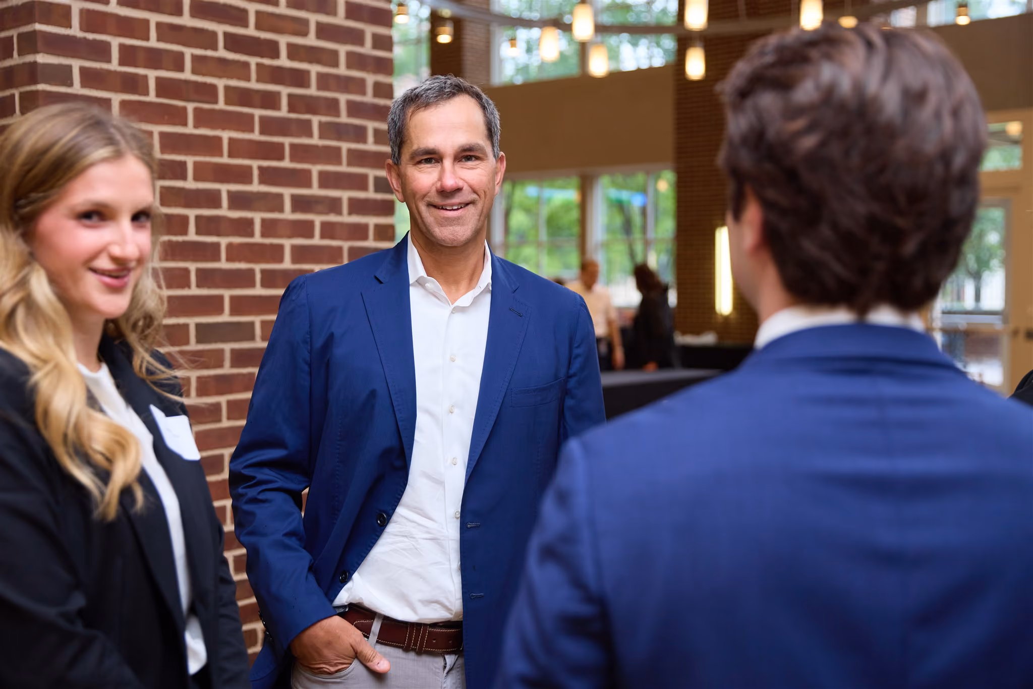 Smiling professional in a navy blazer talking with students at a networking reception