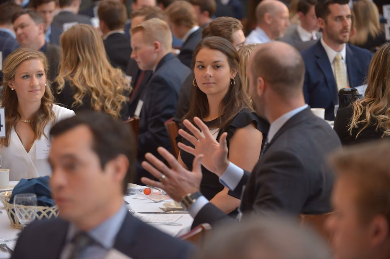 Students and professionals seated at banquet tables listening as a speaker gestures during a luncheon