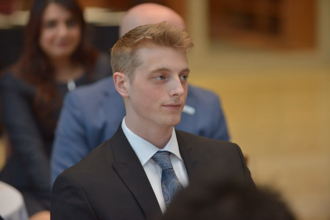 Young man in a suit and blue tie listening attentively at a Scholars of Finance event