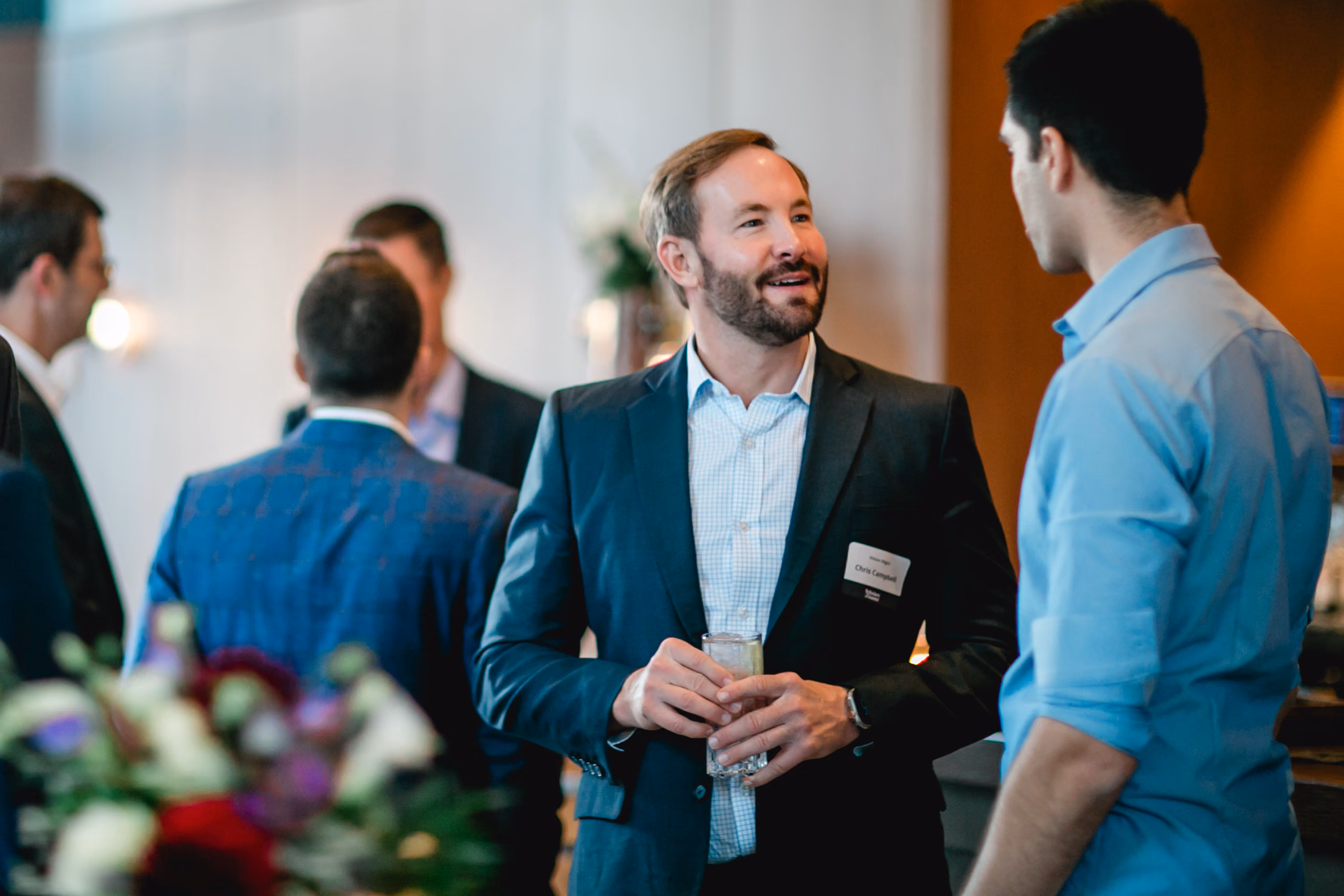 Smiling professional with a name tag talking with a student at an evening networking reception