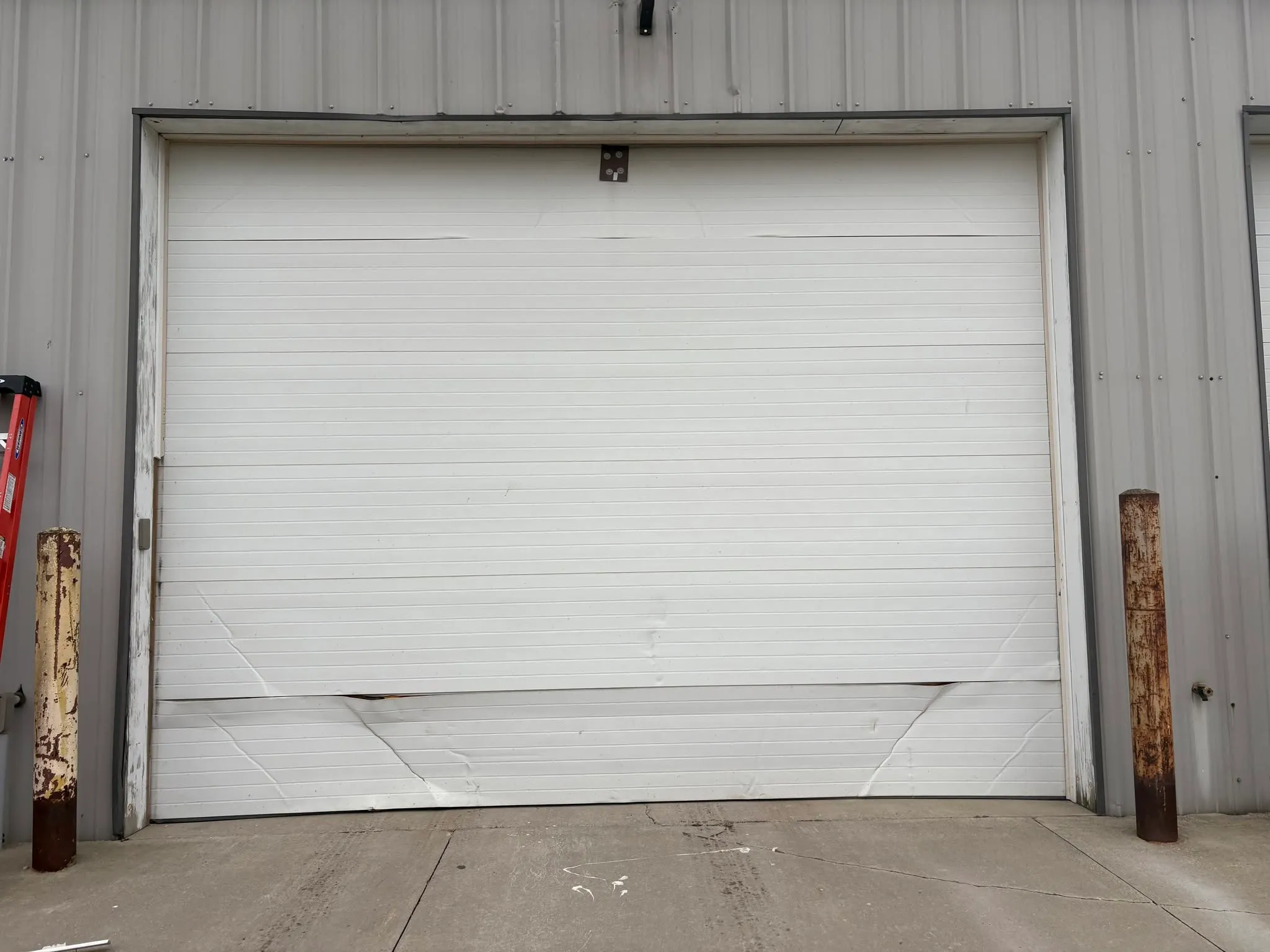White sectional garage door with cracked and dented lower panels.