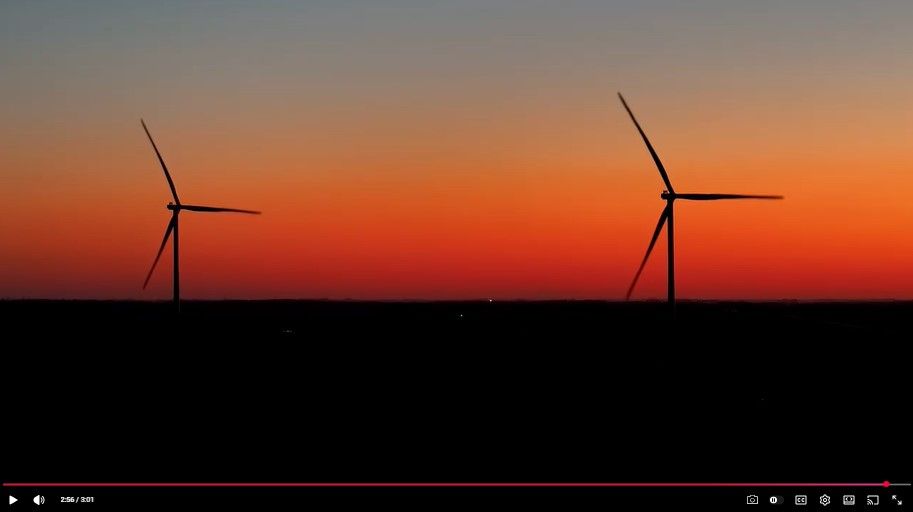 Two wind turbines silhouetted against a vibrant orange and red sunset sky, with a dark horizon below.