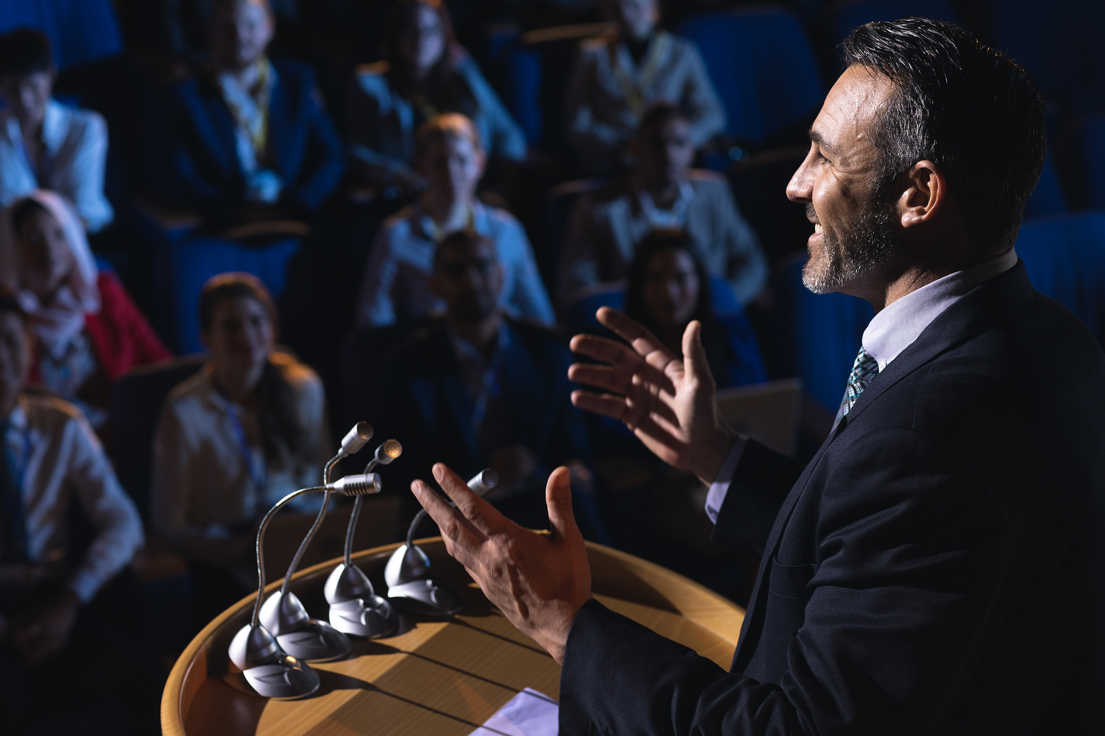 A speaker addressing a seated audience from a podium