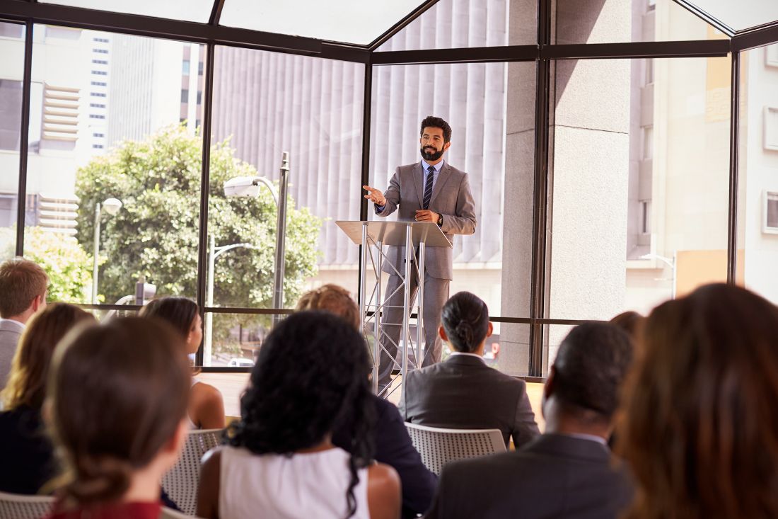 A speaker presenting at a lectern to an engaged audience