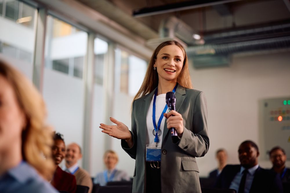 A professional speaking into a microphone to an engaged audience