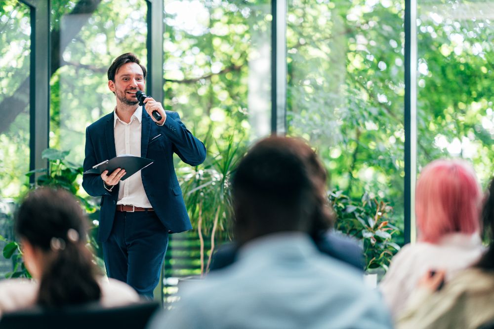 A speaker addressing a seated audience with a microphone