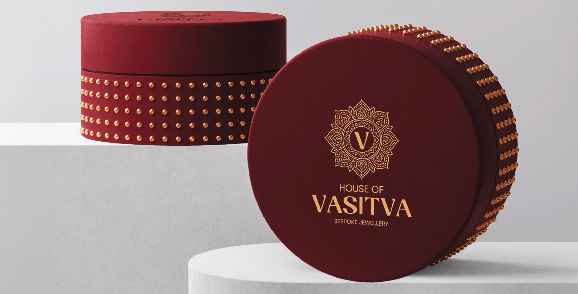 Two round maroon boxes adorned with gold studs and House of VASITVA bespoke jewellery logo on one box.