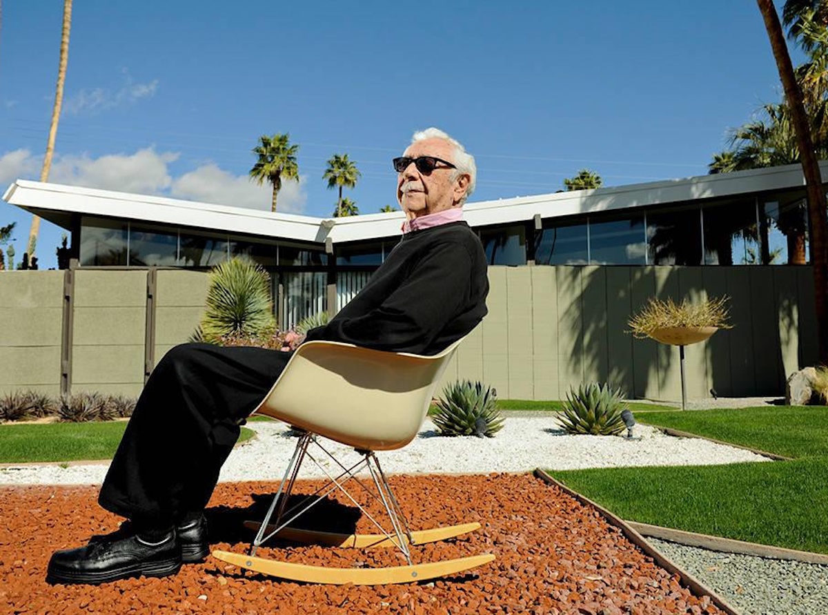 Max seated in a rocking chair in front of a mid-century house with a butterfly roof