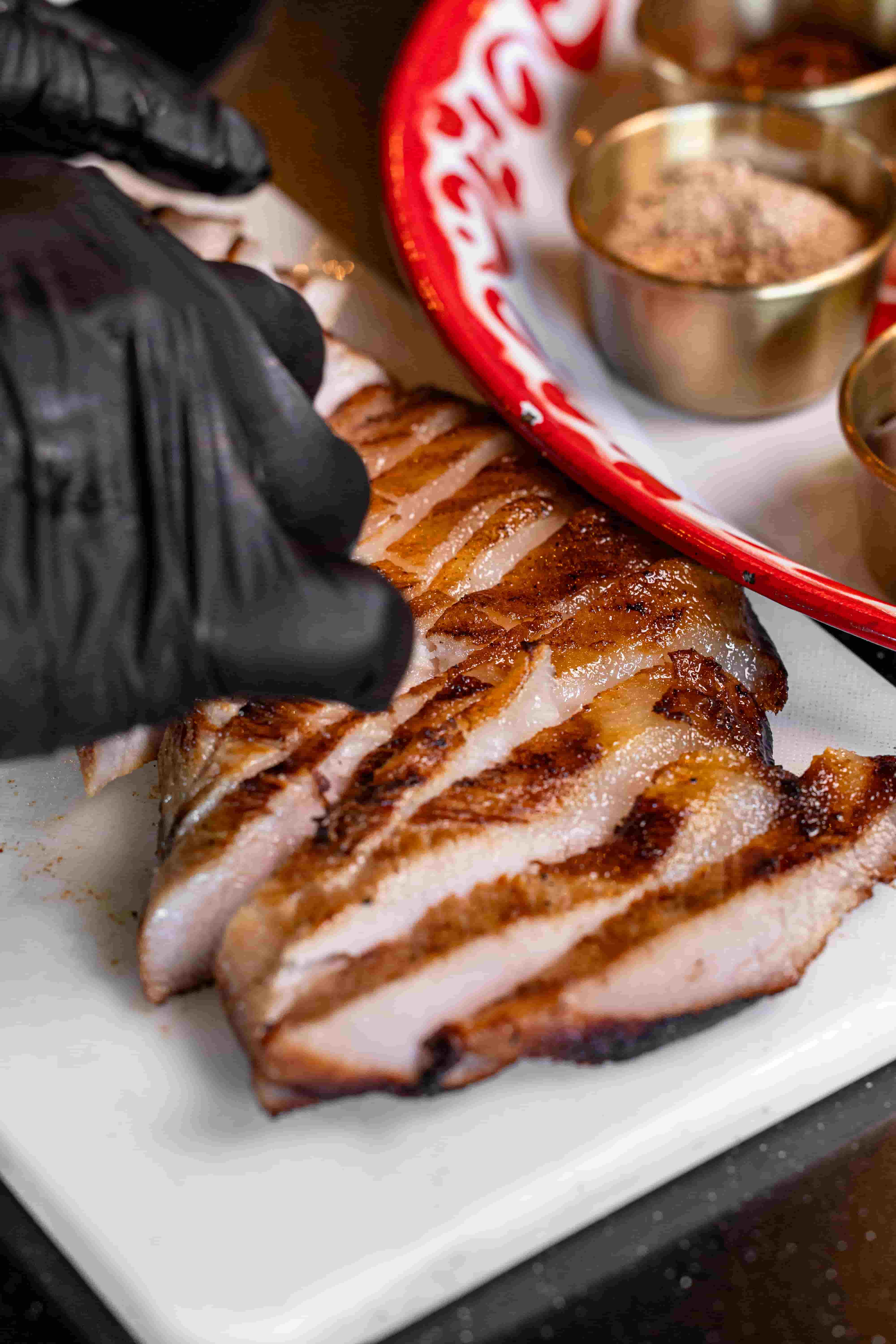 Close up of sliced grilled pork belly with dark char marks on a white cutting board