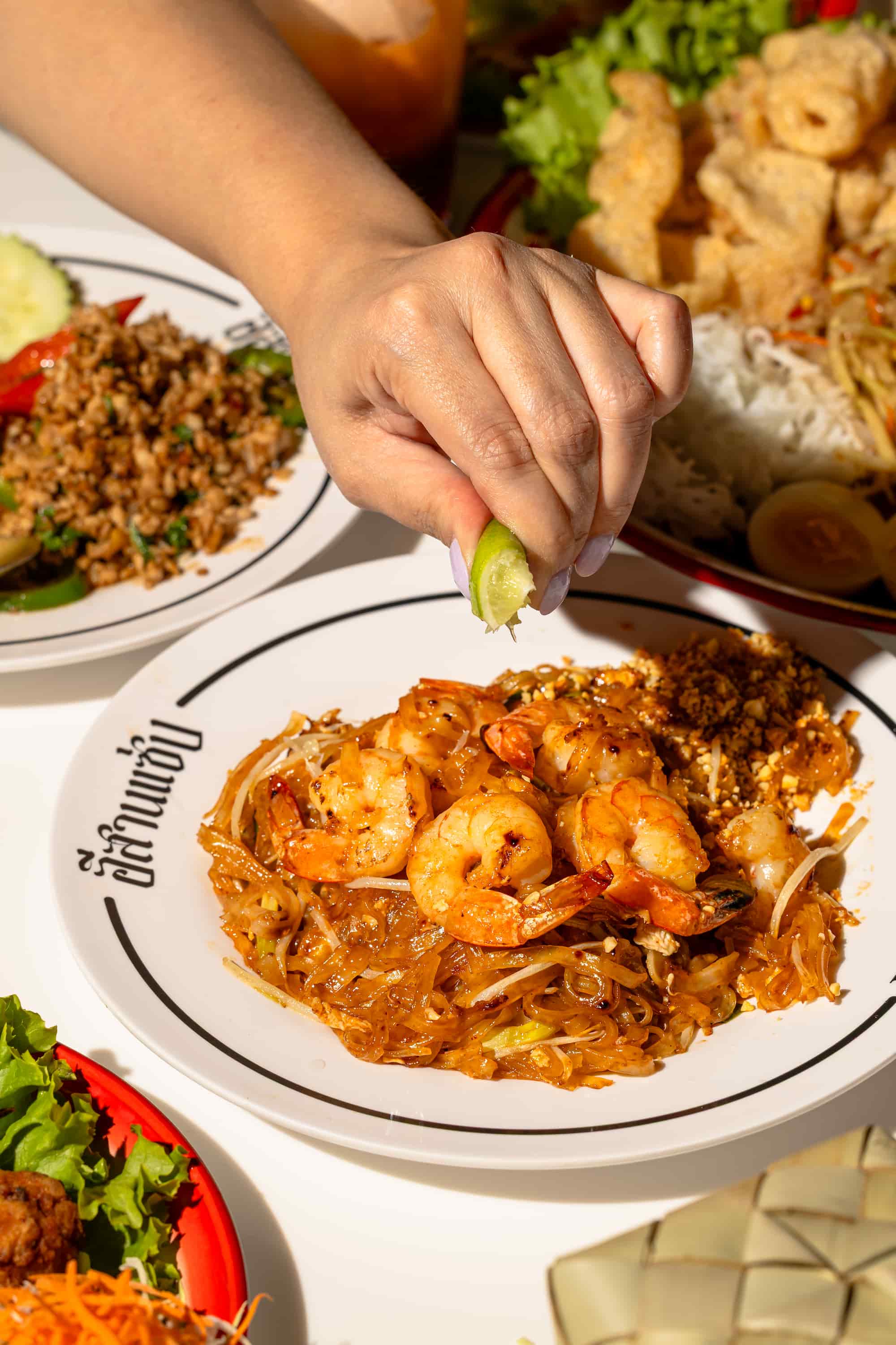 Hand squeezing lime over a plate of shrimp pad thai with bean sprouts and crushed peanuts