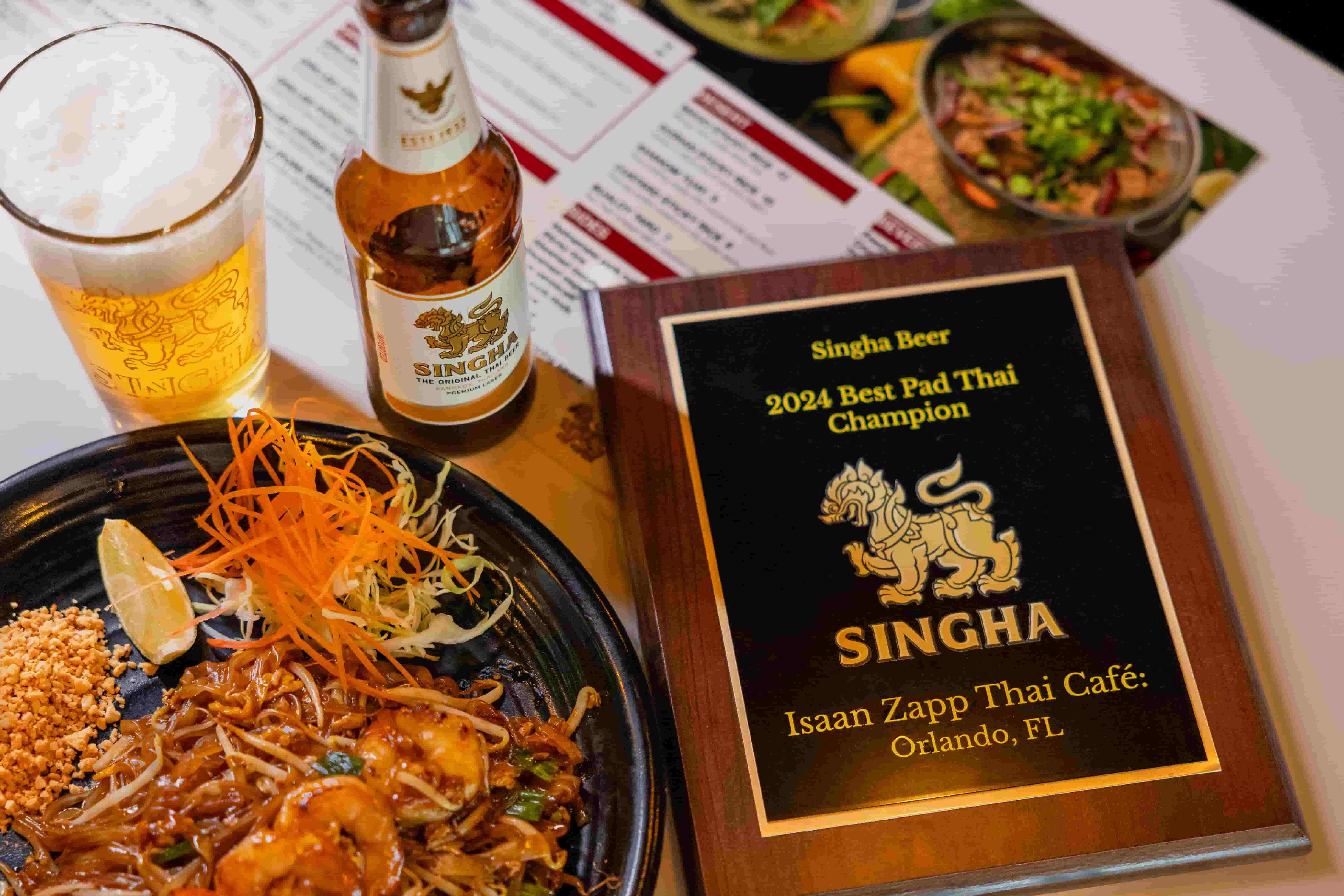 Singha 2024 Best Pad Thai Champion plaque beside a plate of pad thai and a cold beer