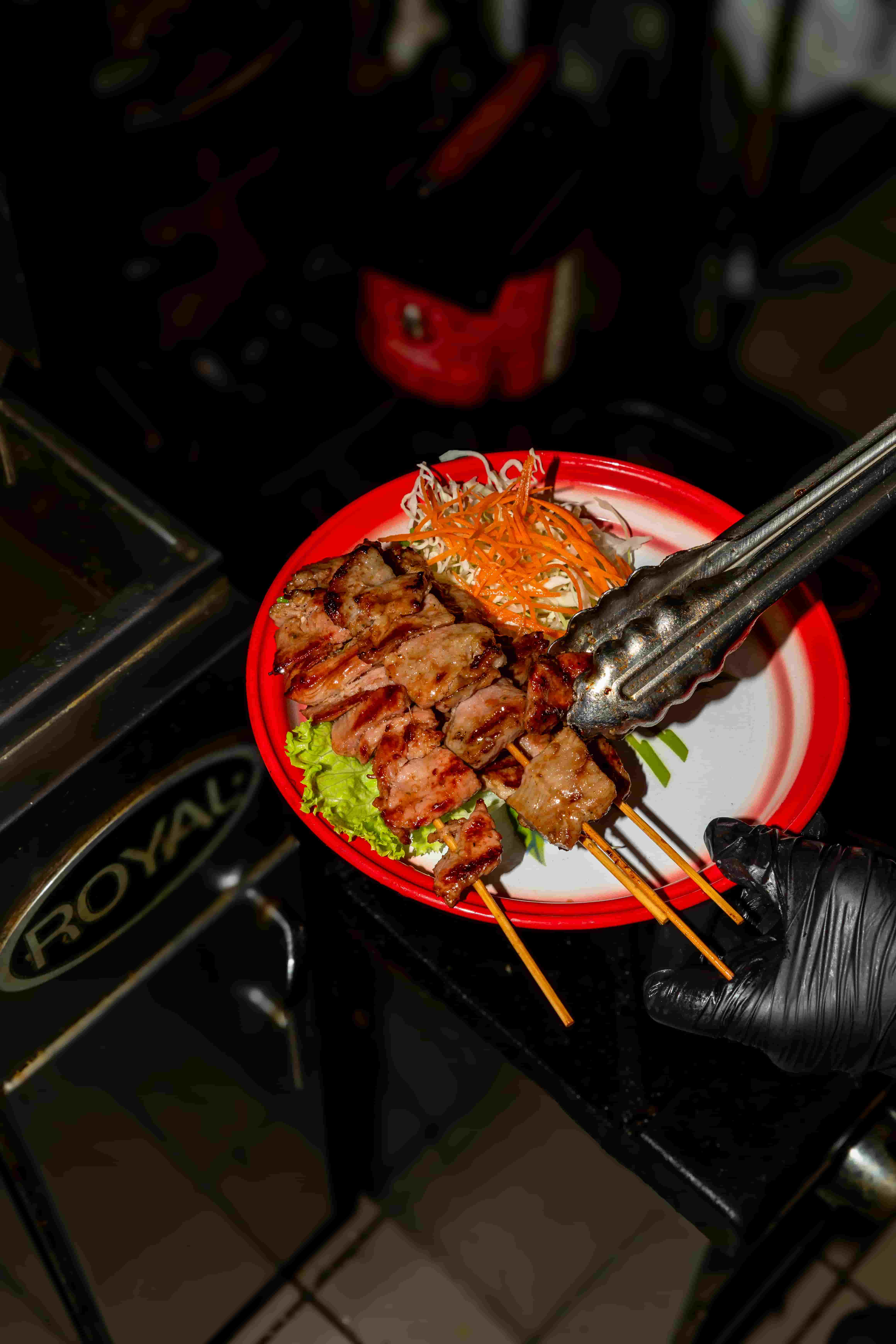 Grilled pork skewers on a red plate with shredded papaya and lettuce, lifted with tongs
