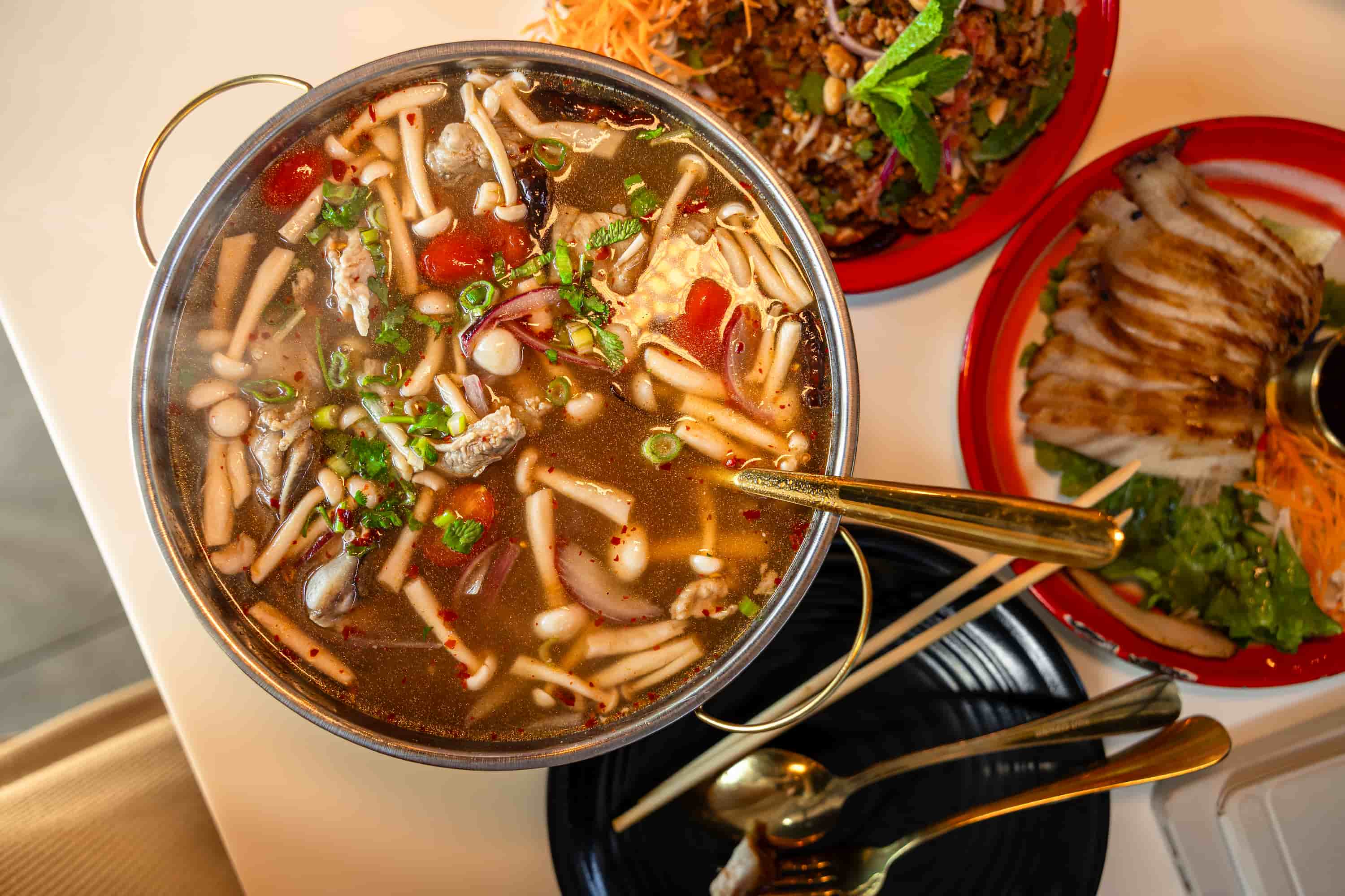 Overhead view of a steaming herb soup with mushrooms, tomatoes and red onion in a metal pot