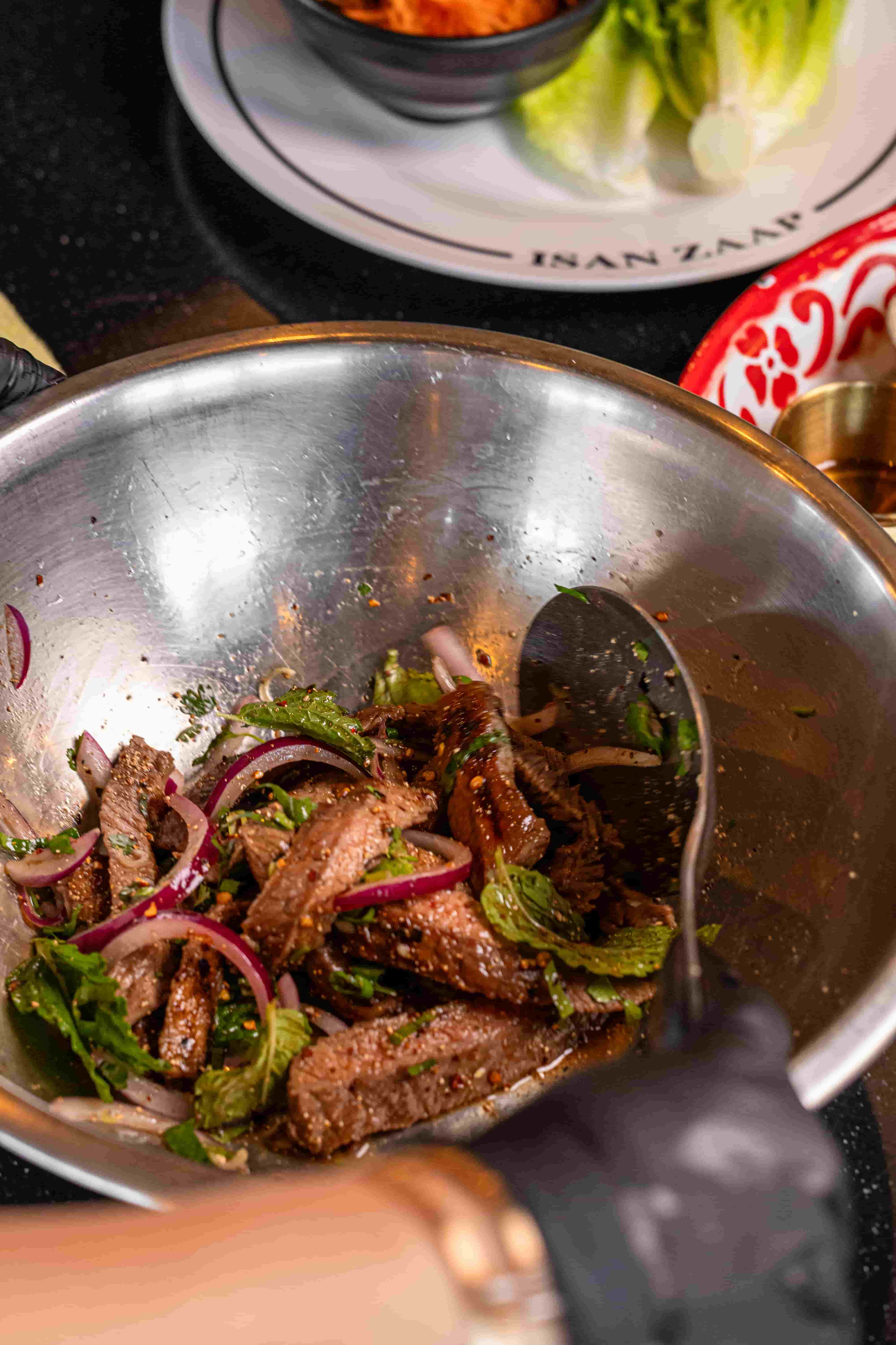Sliced grilled beef tossed with red onion, mint and chili flakes in a steel mixing bowl