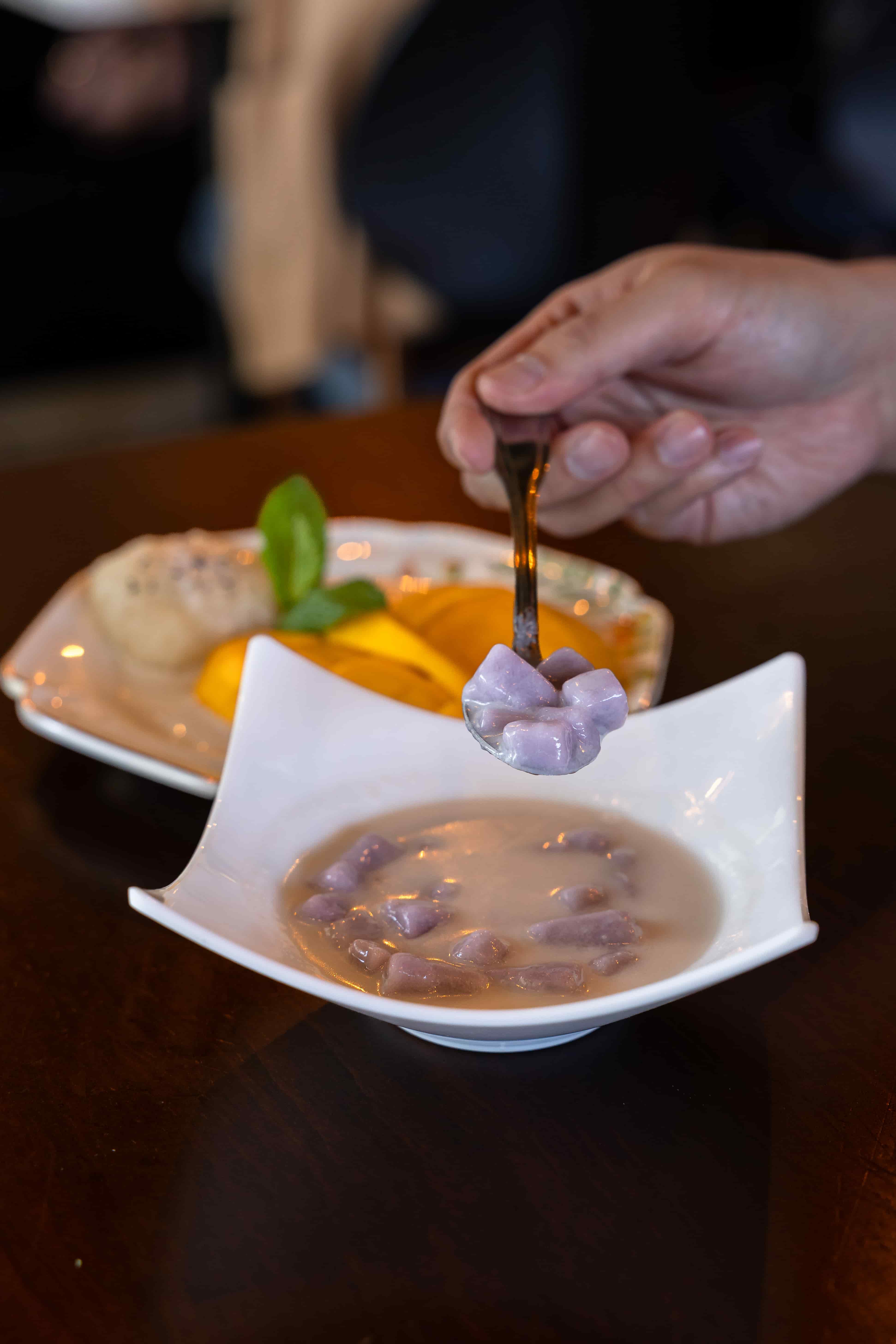Spoonful of purple taro balls in warm coconut milk, with mango sticky rice behind