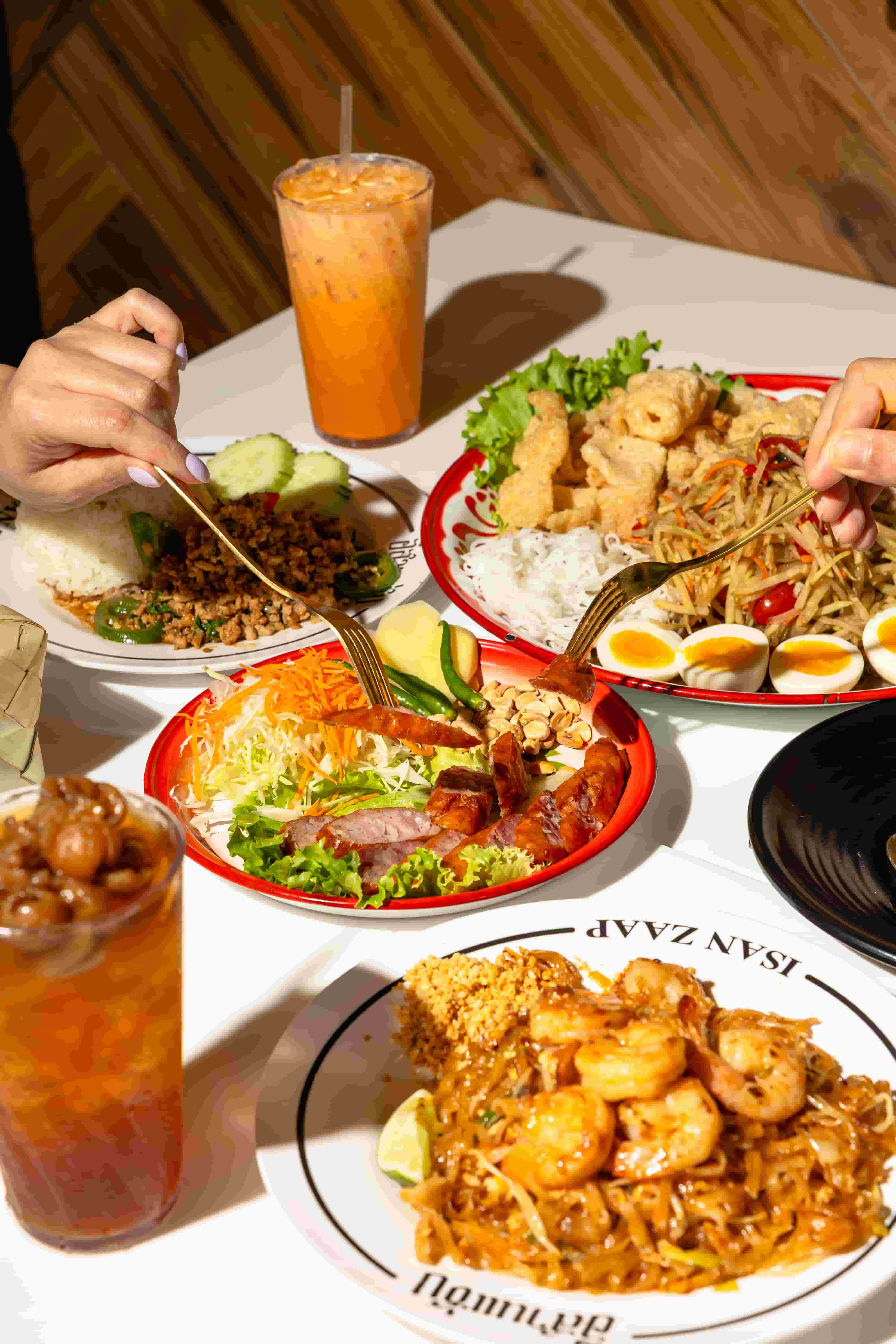 Table spread of green papaya salad, pad thai with shrimp, minced pork and two iced teas