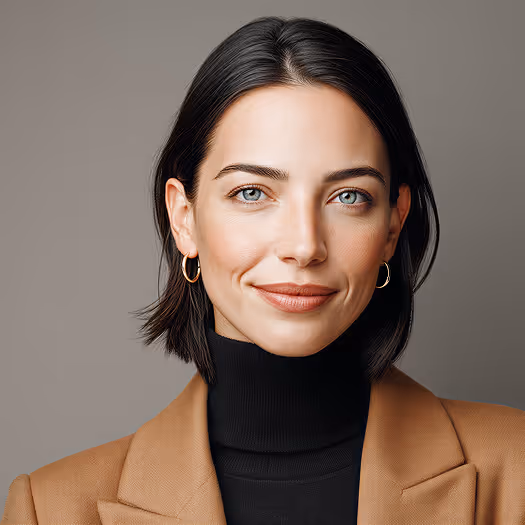 Portrait of a woman with short dark hair wearing gold hoop earrings, a black turtleneck, and a brown blazer, smiling softly against a neutral background.