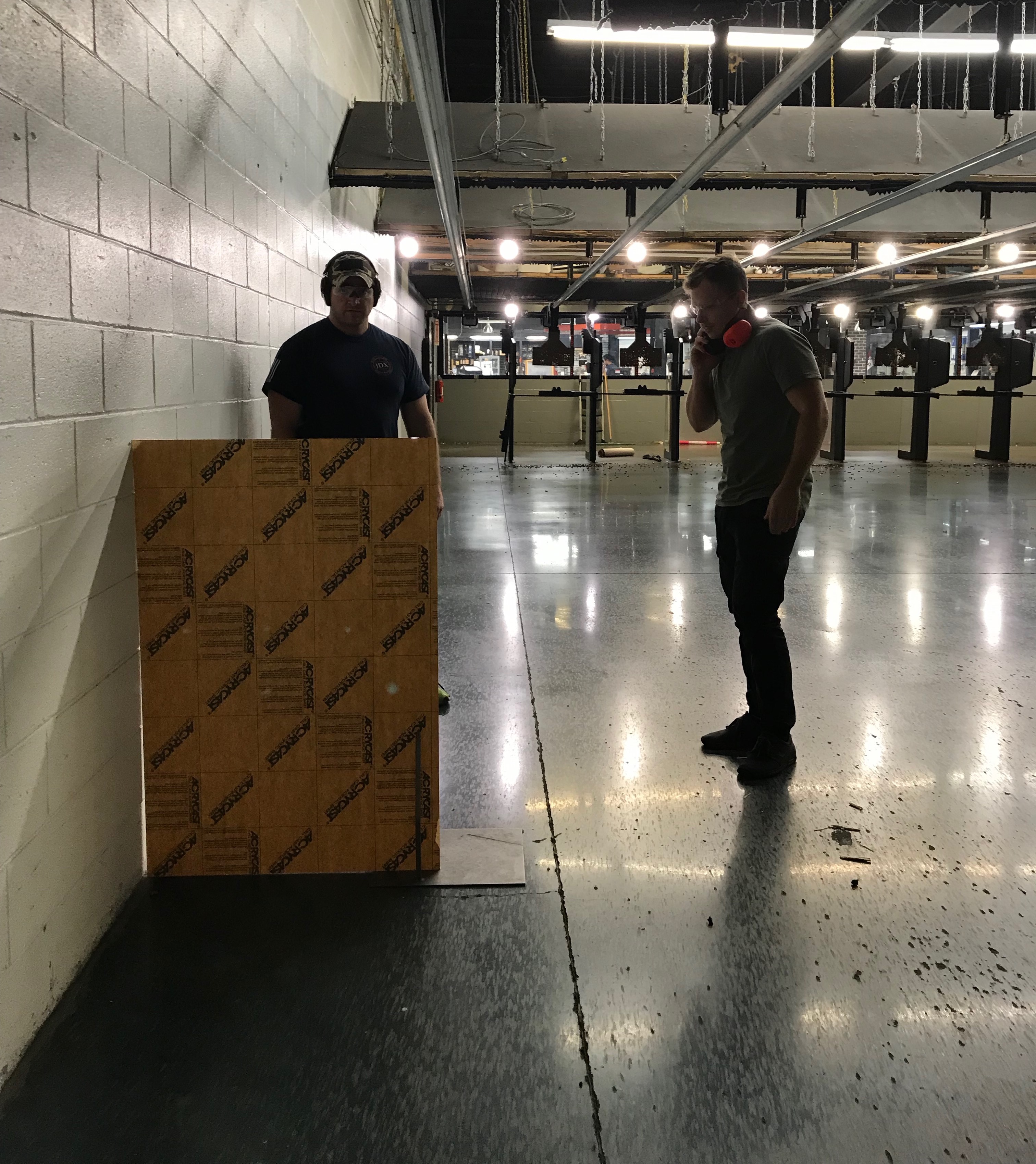 The acrylic sheet in a cardboard backing, standing at an indoor range, with two people beside it.