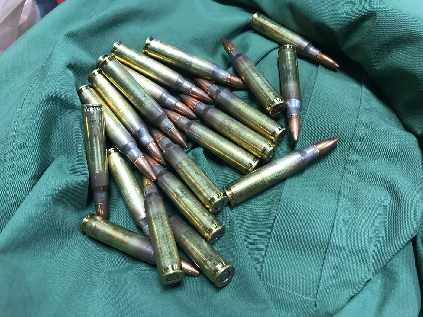 A handful of brass rifle cartridges on a green cloth.