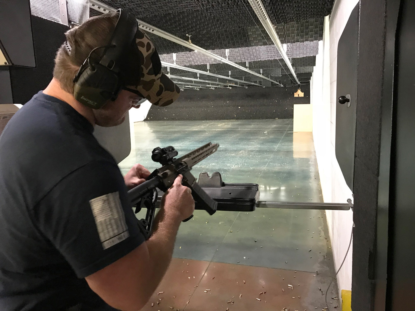 A shooter in ear protection handles an AR-15 rifle in an indoor range lane.