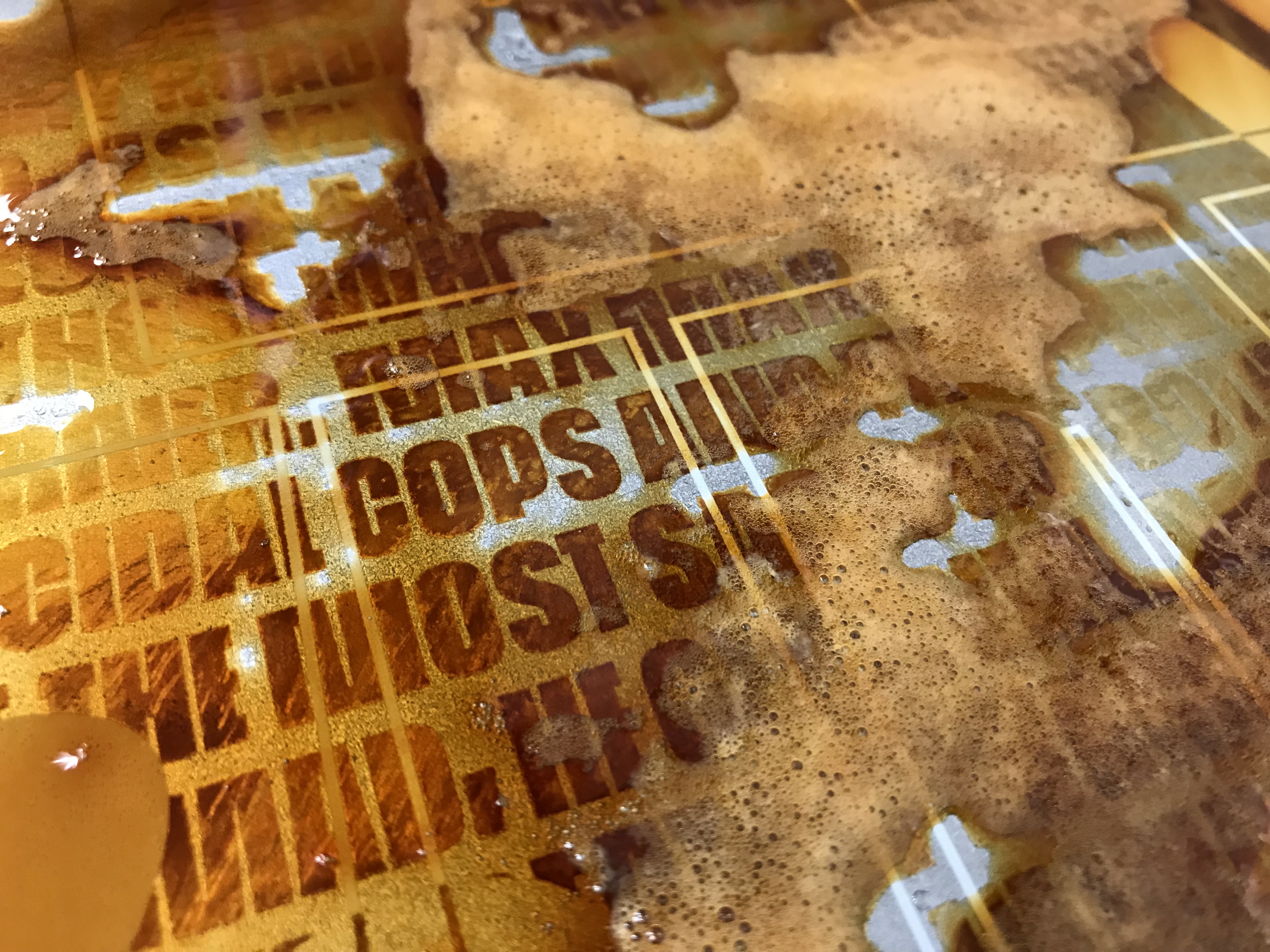 A wet, rusting plate: bright orange rust and pools of solution around white letters and clear-masked text.