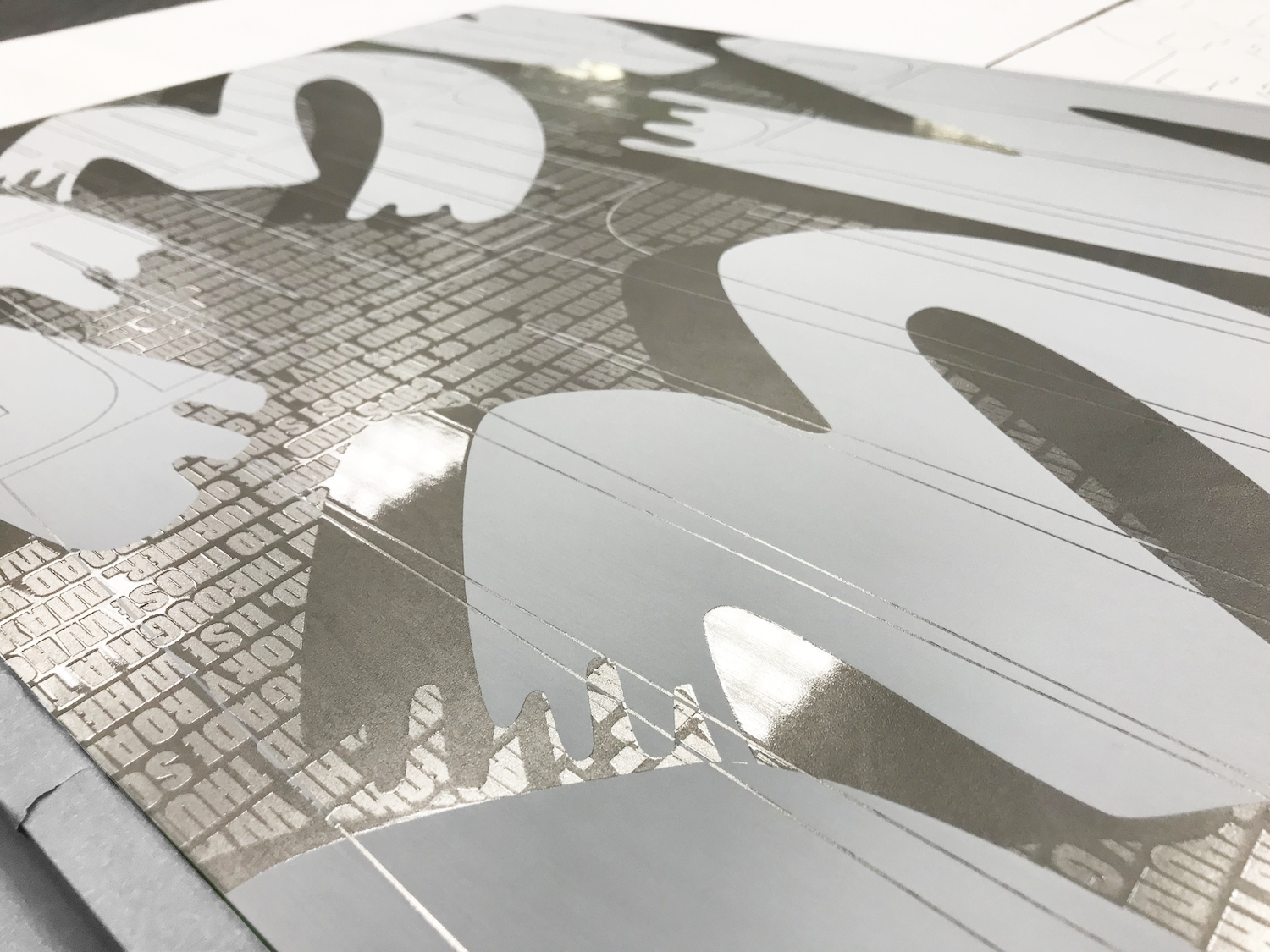Close-up of the printed plate: white letterforms and a grid of tiny clear-ink text on bare, shiny steel.