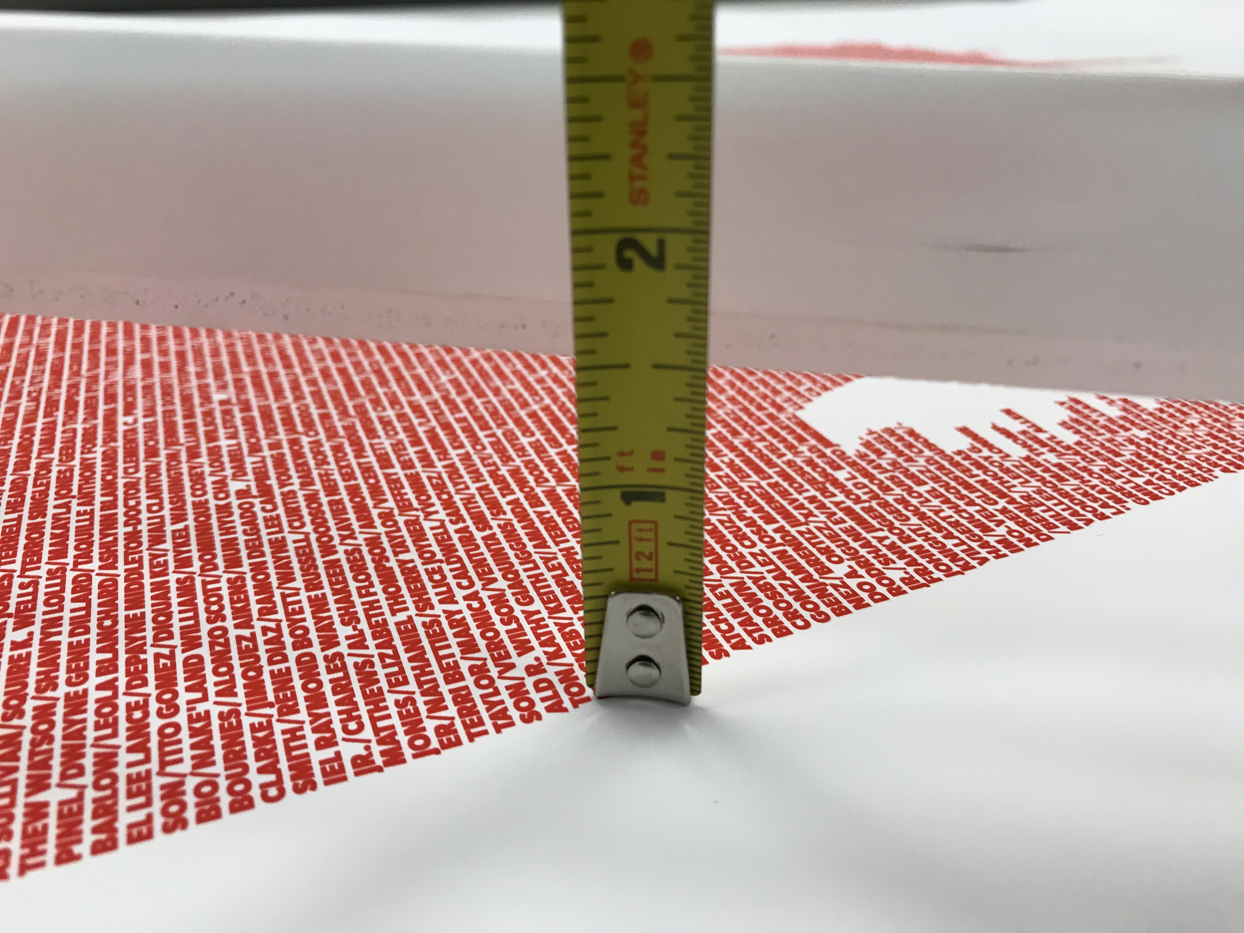 A tape measure laid across the printed back image: rows of names in bold red capitals.