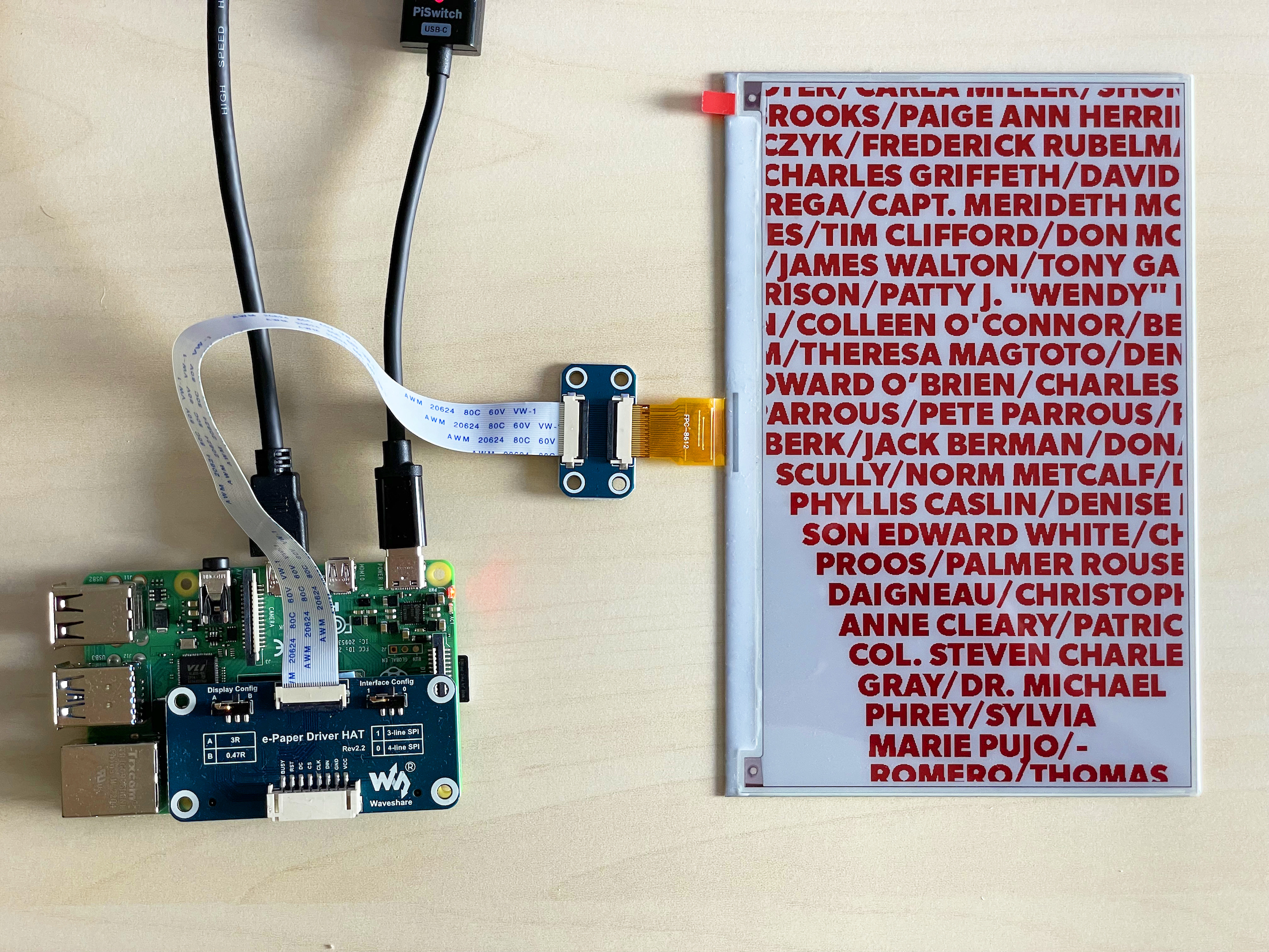 A Raspberry Pi wired to a three-colour e-paper display showing rows of names in red and black.