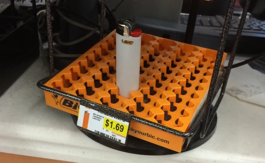 An orange Bic display tray on a shop counter, empty except for a single white lighter, with a $1.69 price tag on its front.