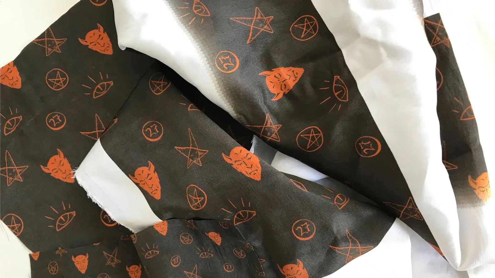 Dark brown silk printed with orange devils, pentagrams, eyes and 27s, lying in folds.
