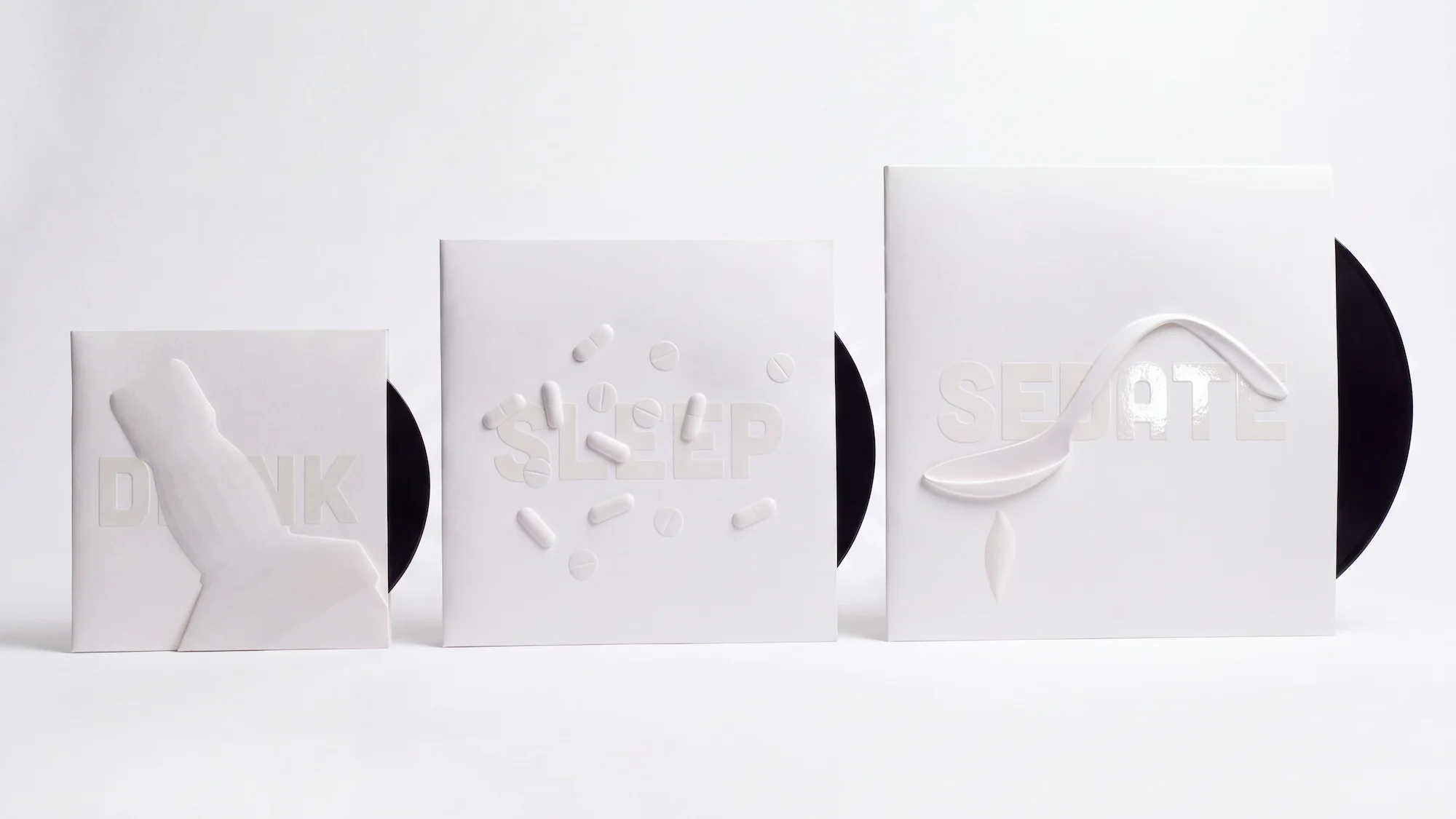 The three white record sleeves in a row, smallest to largest: DRINK with a raised bottle, SLEEP with pills and SEDATE with a spoon, a black record peeking out of each.