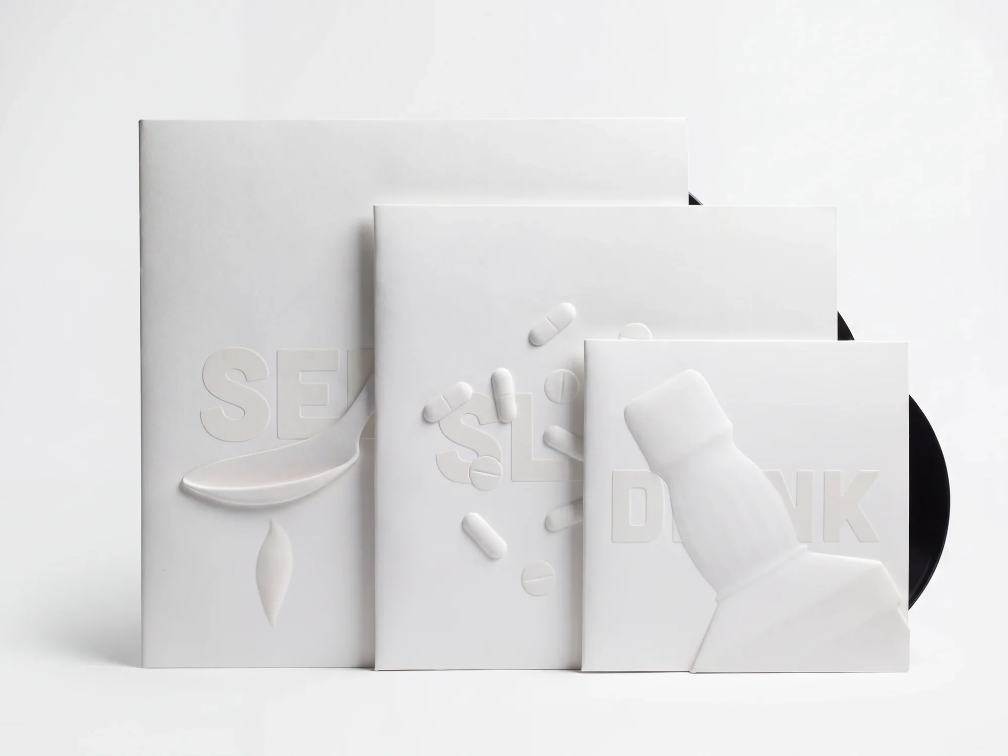 All three sleeves, overlapping from the 12-inch SEDATE at the back to the 7-inch DRINK in front, a black record peeking out behind.