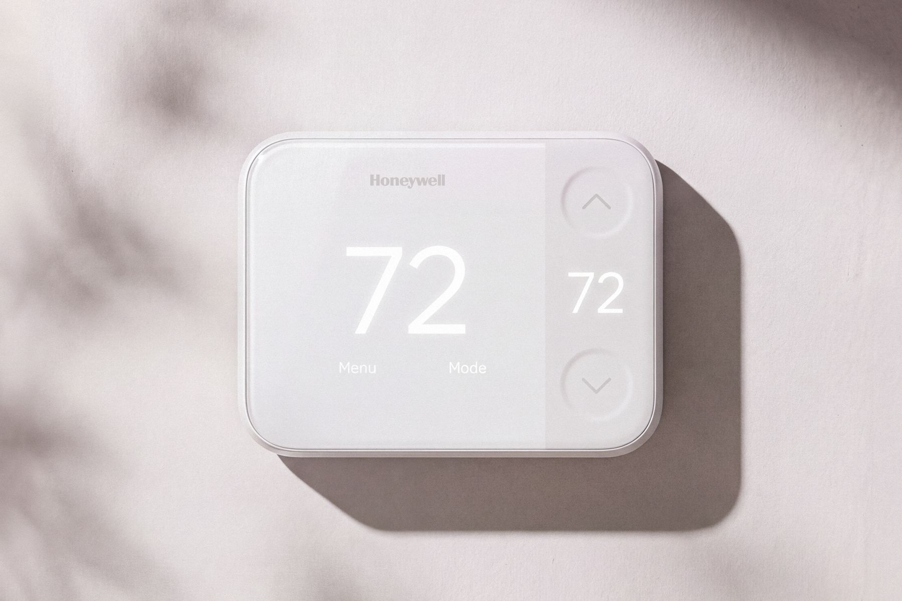 A white Honeywell thermostat on a softly shadowed wall. A large 72 glows through the cover, with Menu and Mode labels below and up and down controls in a textured strip on the right.