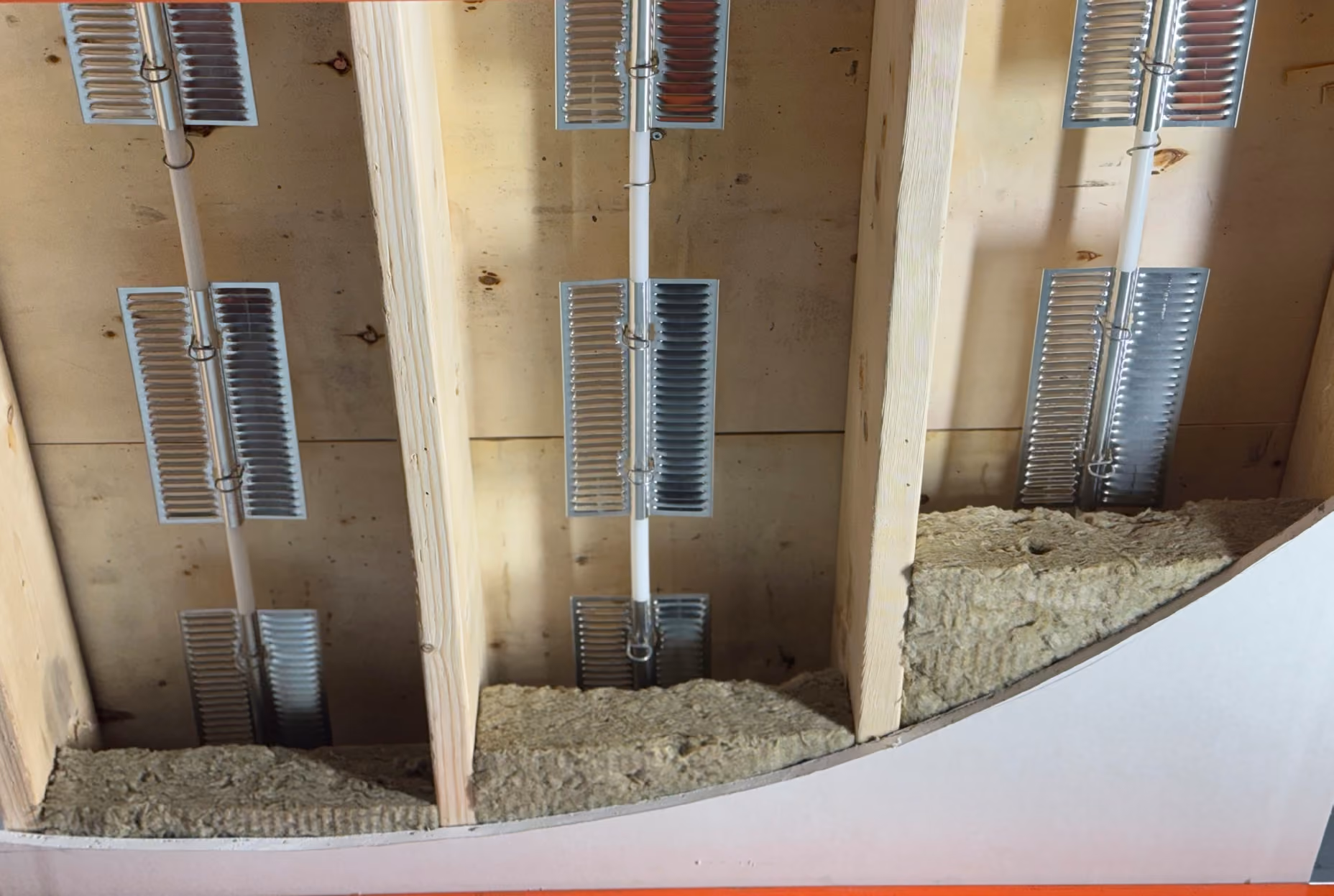 Ceiling joists with metal electrical clamps and insulation foam between the wooden beams.