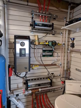 Wall-mounted plumbing system with valves, gauges, pipes, and control units in a utility room.