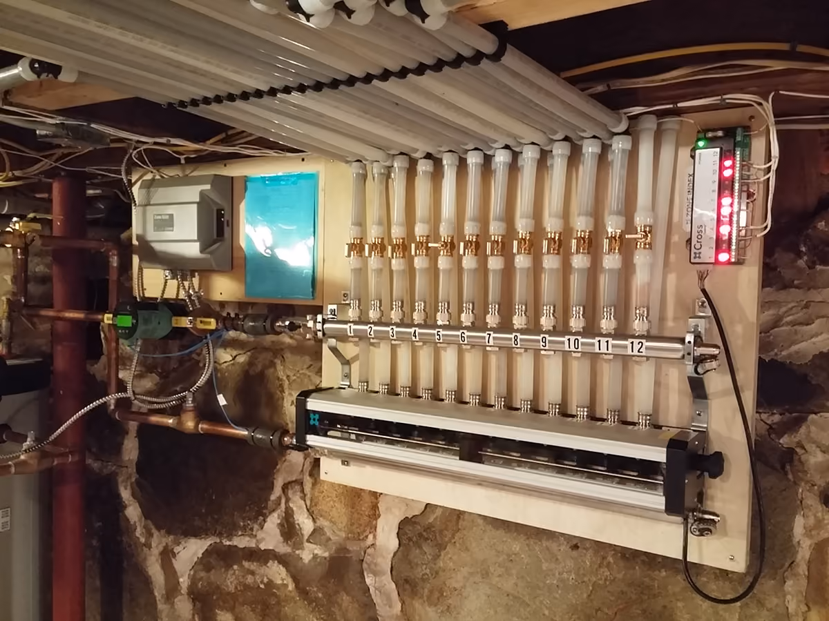 Basement wall with a hydronic radiant floor heating manifold and numbered valves under pipes.
