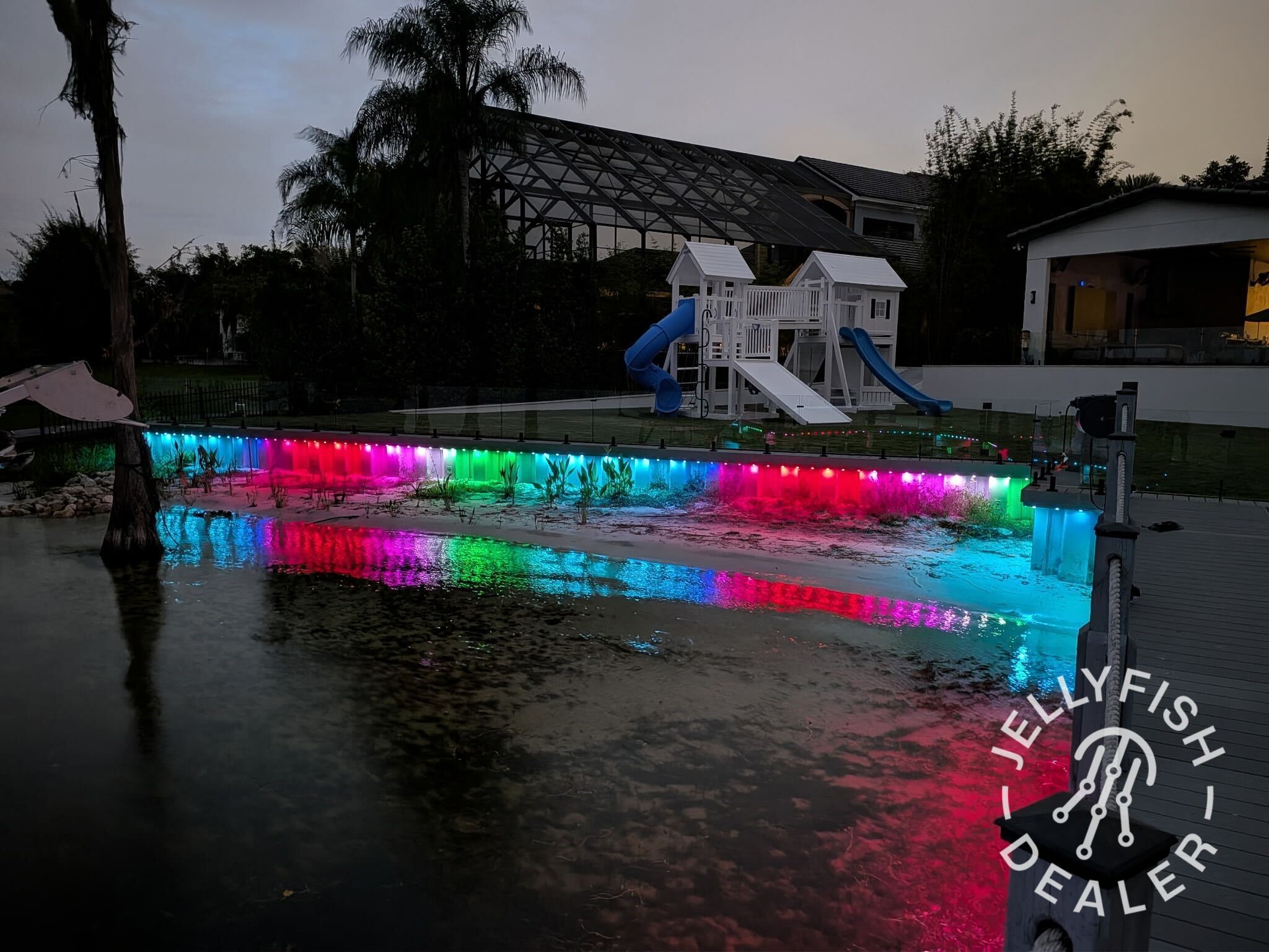 Color-changing JellyFish lights along a waterfront dock and shoreline at dusk.