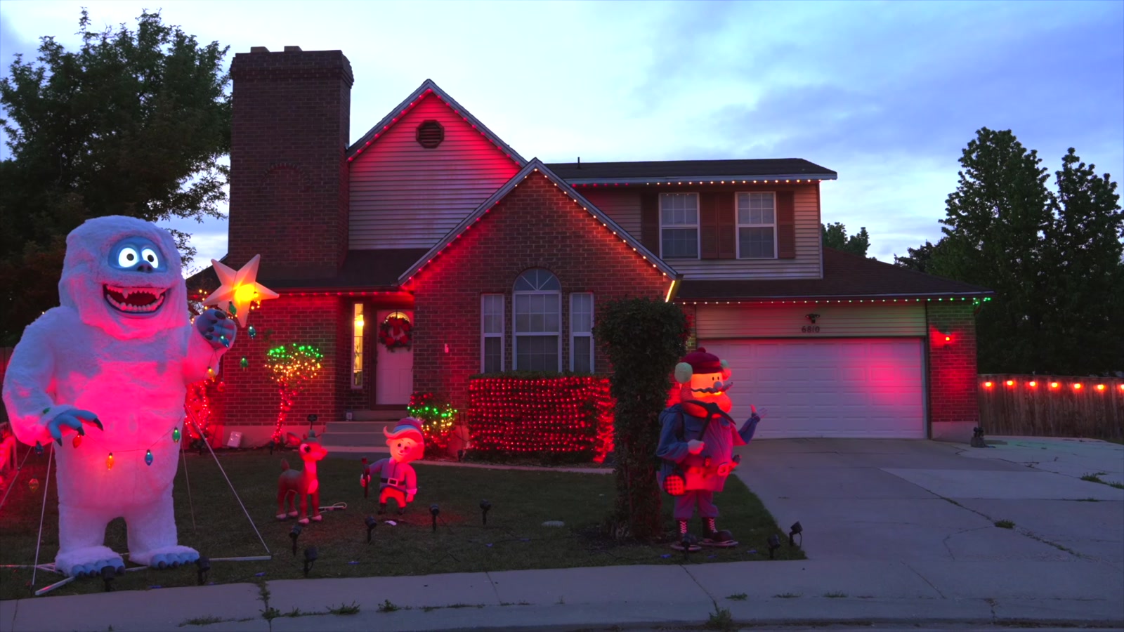 Christmas string lights wrapped around shrubs beside a decorated entrance