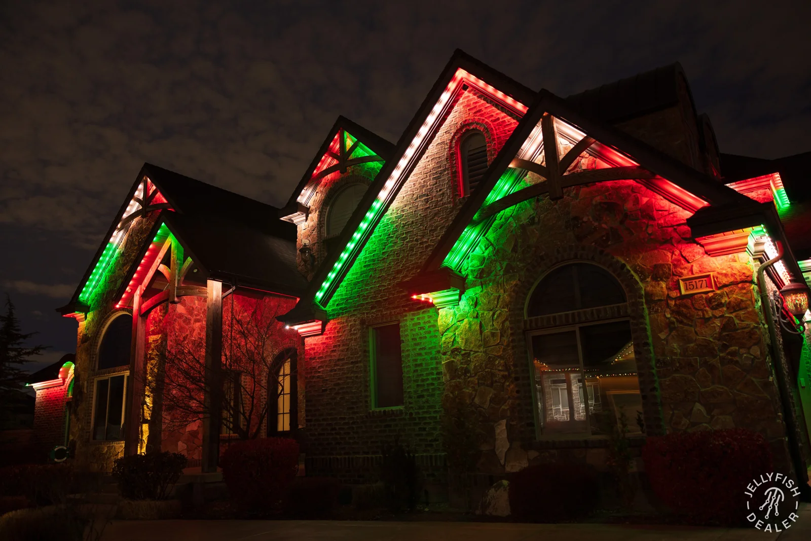 Red and green Christmas lights outlining a stone home.