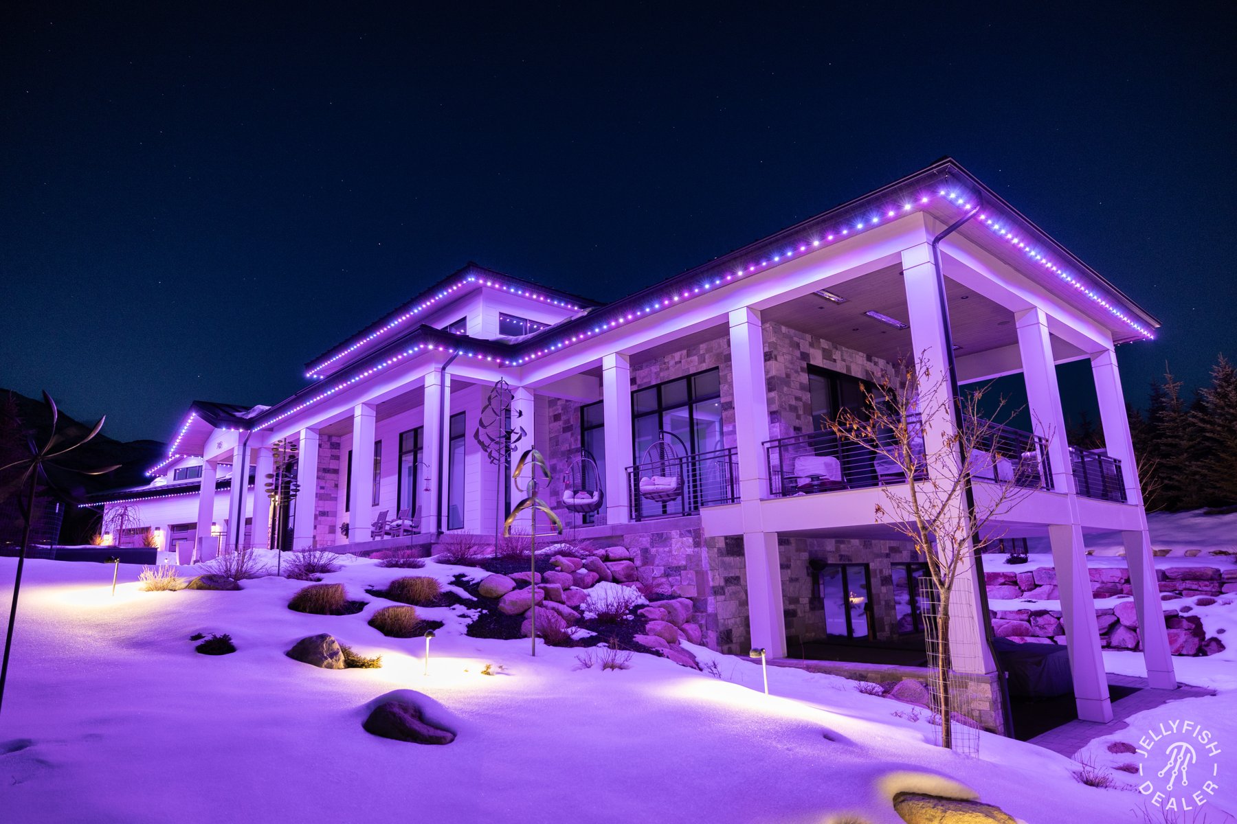 Pink and purple lighting across a snow-covered modern home.