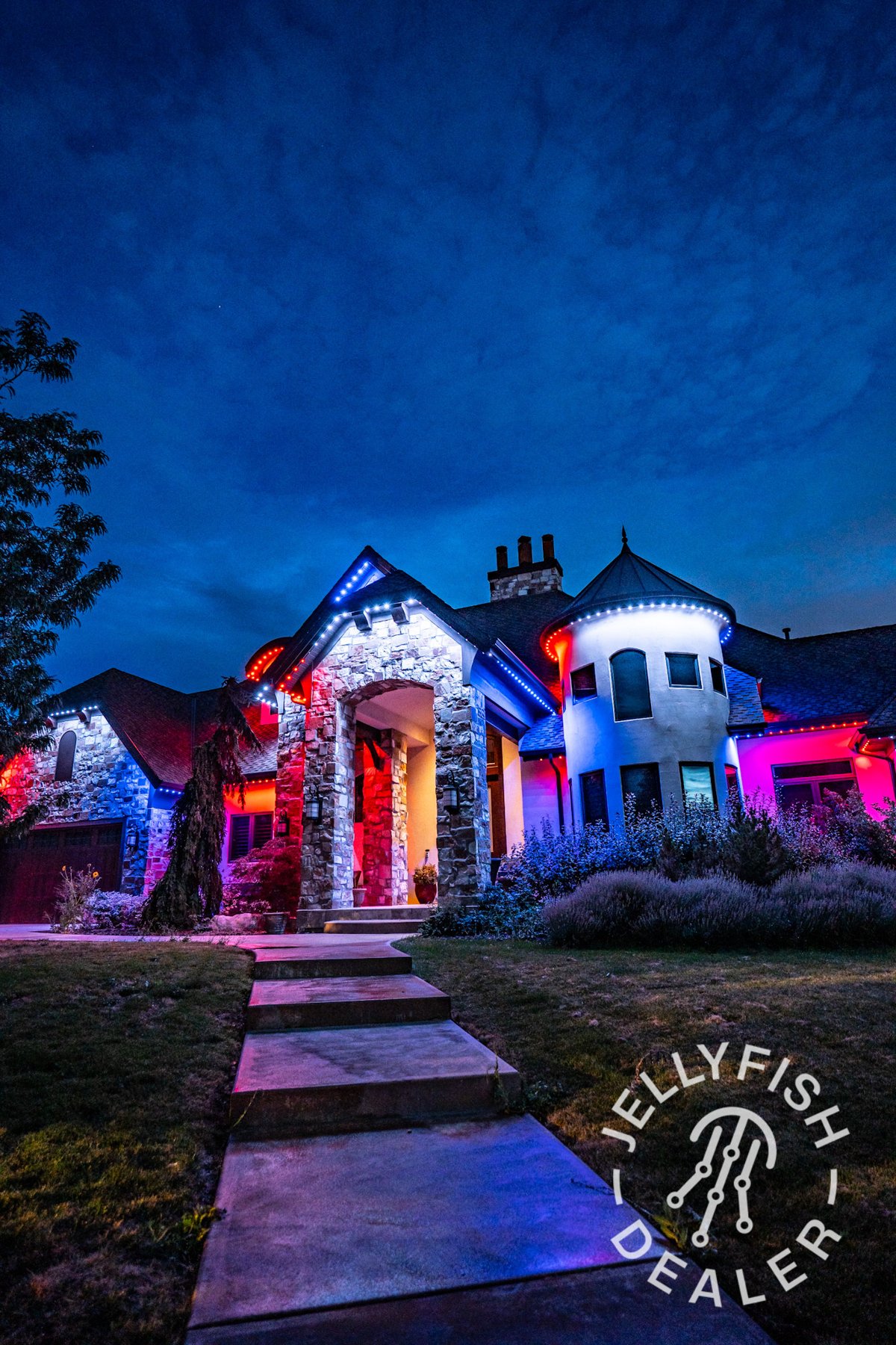 Red, white and blue lighting on a stone home with a front walkway.