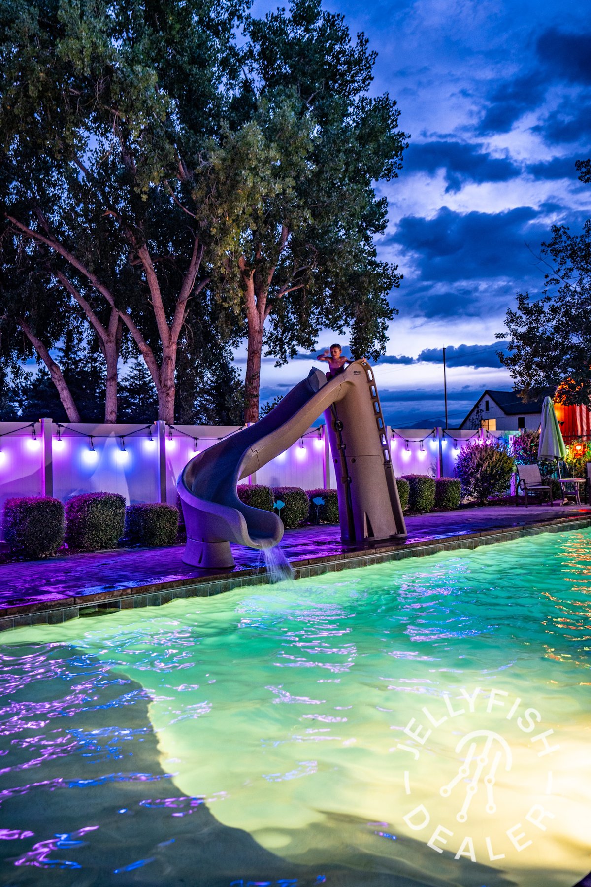 Colored patio lighting beside a landscaped swimming pool.
