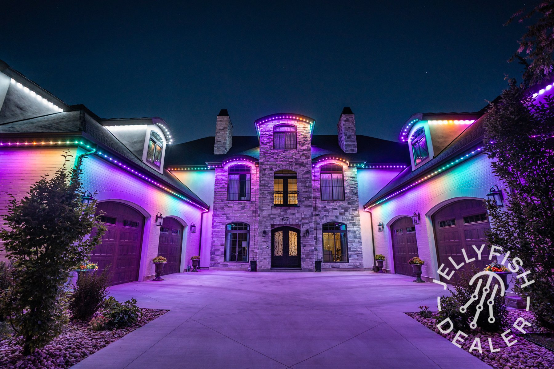 Multicolor roofline lighting across a stone home at night.