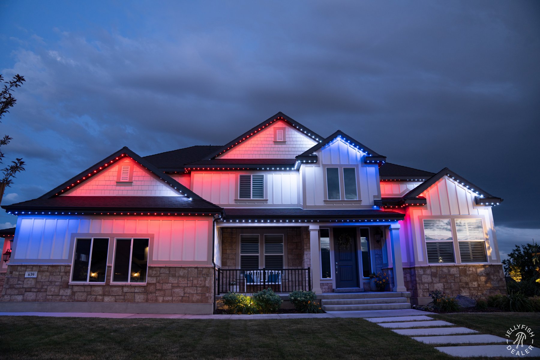 Patriotic roofline lighting on a white and stone home.